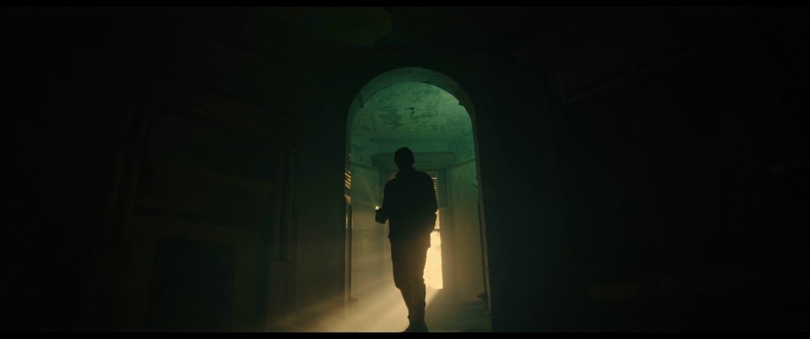 Production still — silhouette in an archway lit by a torch beam