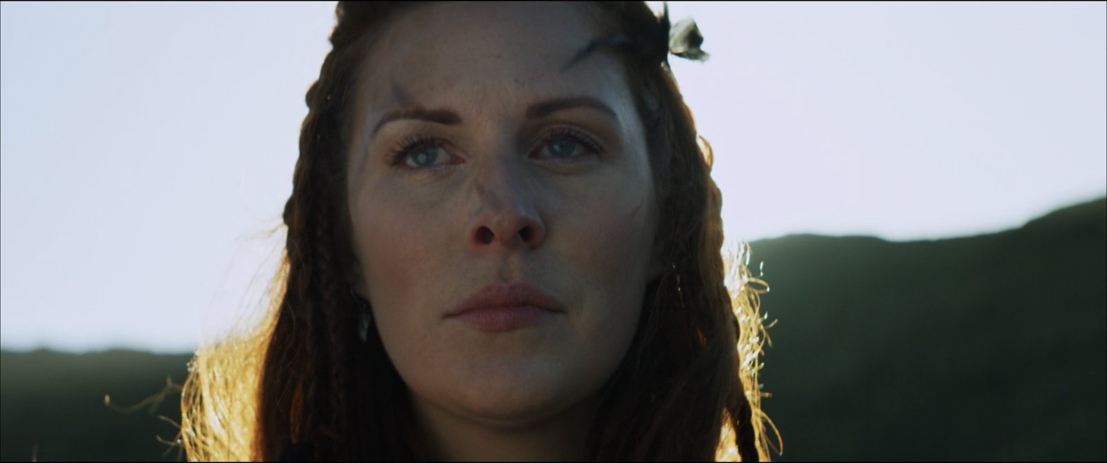 Production still — woman backlit against hills at golden hour