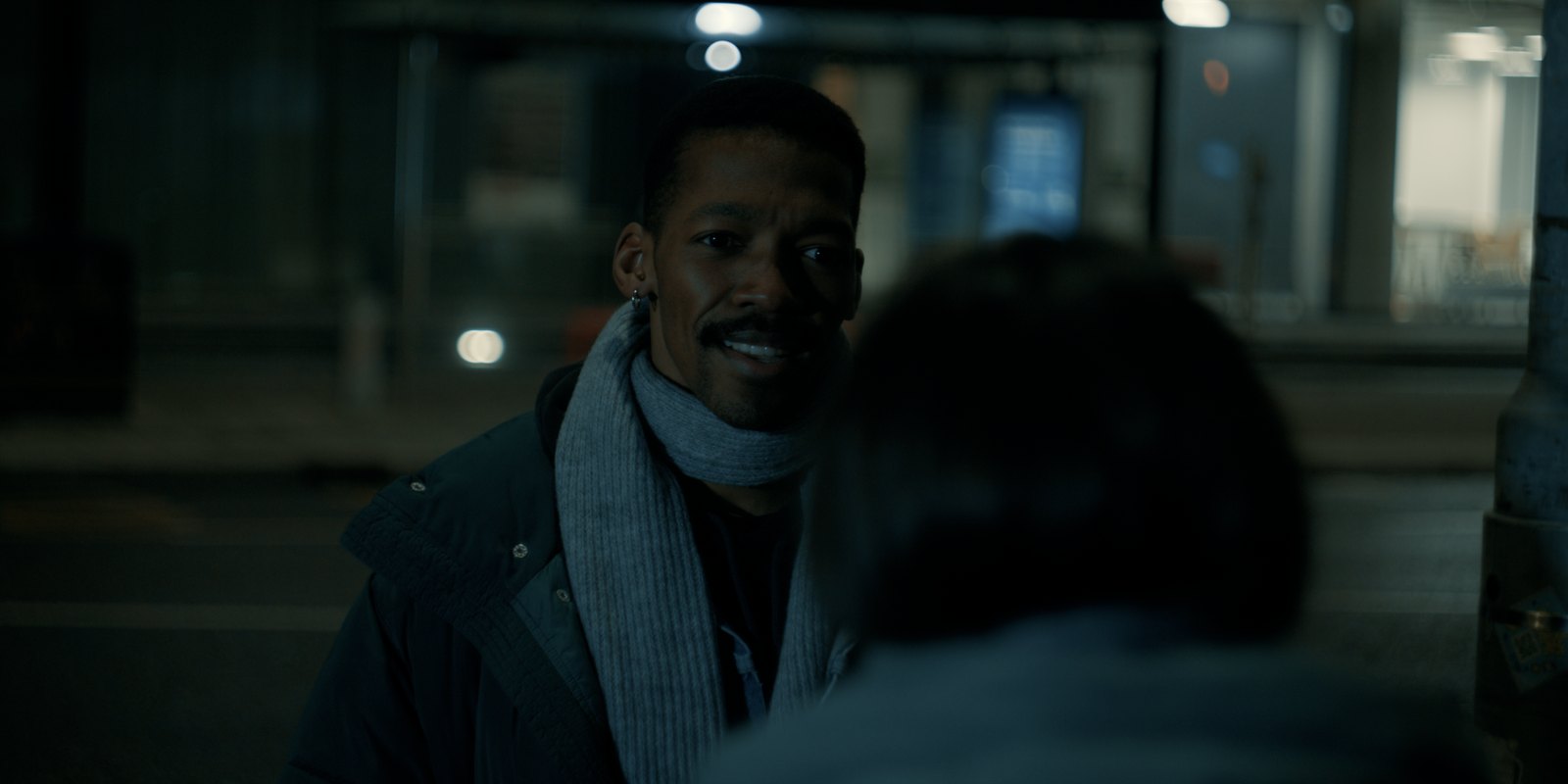 Production still — two-shot at a bus shelter at night