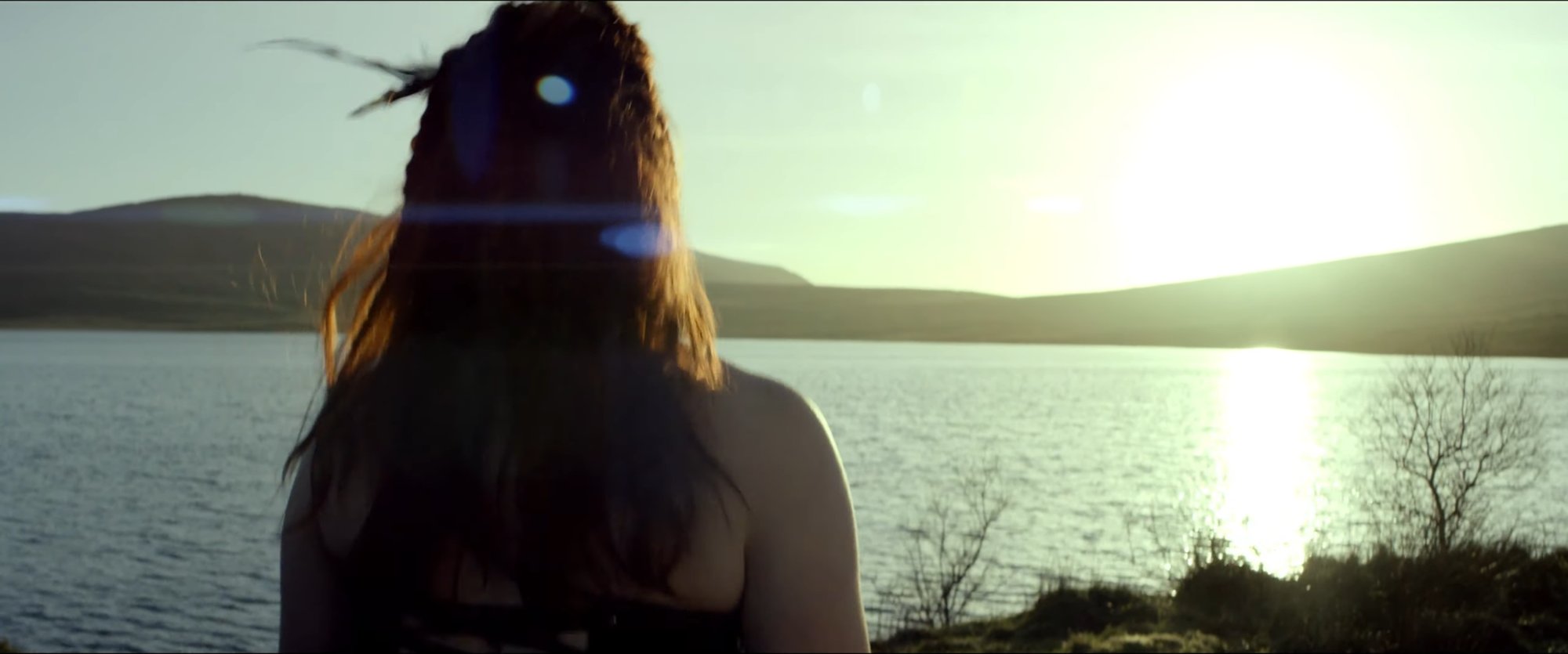 Production still — figure at a lake at golden hour