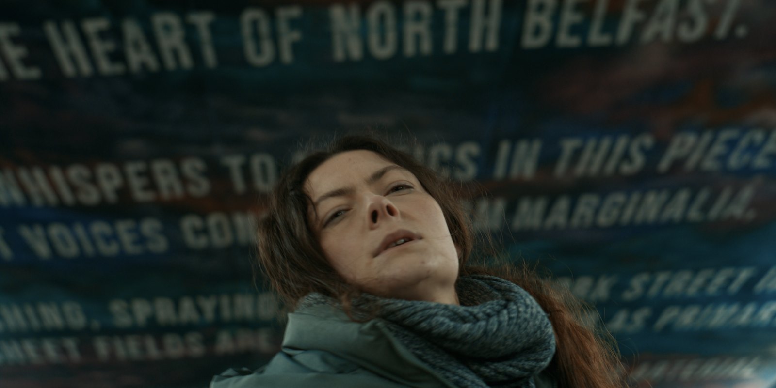 Production still — woman against a painted mural wall